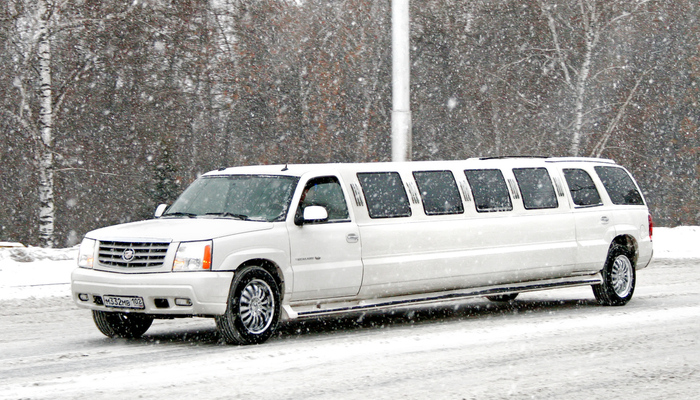 White Cadillac Escalade limousine at the city street in the snow at Christmas season