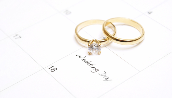 A note on a calendar sets a reminder for the wedding day with couple gold rings on top