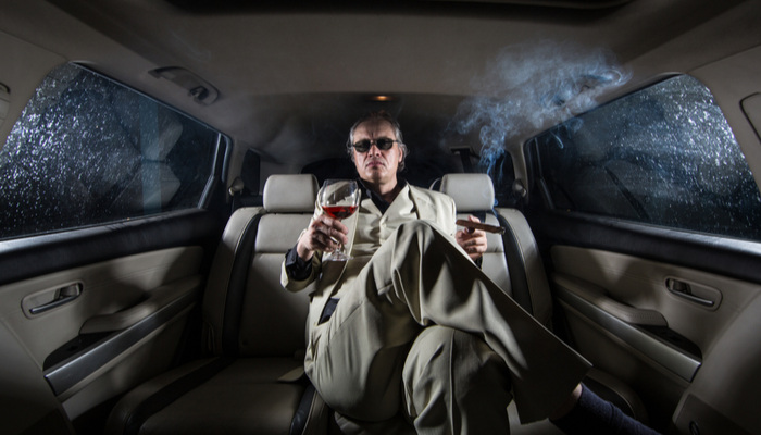 Rich man in a white suit and a cigar with a glass of wine in a luxurious limousine