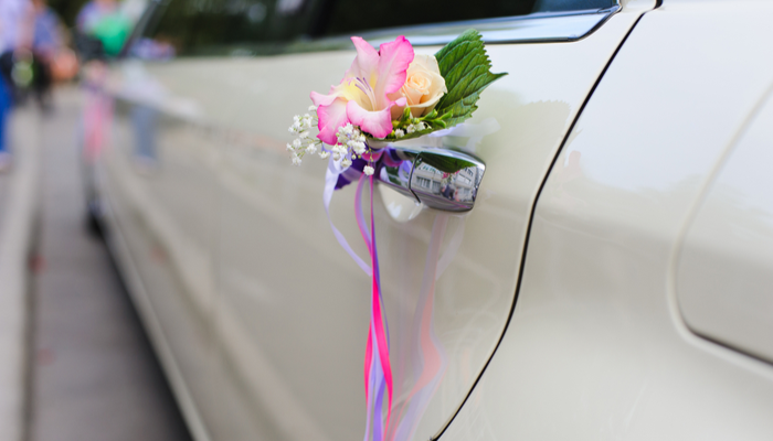 Spring vibes wedding decor on the car handle. Flower decoration with pink ribbons on a white limousine