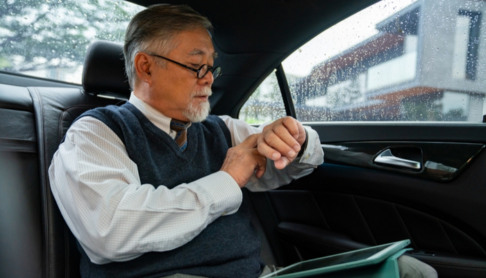 Confidence senior businessman in suit sitting on limousine car backseat working on digital tablet checking time on hand watch while going to office.png